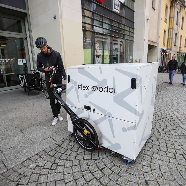 Big, white aluminium container being released from a BicyLift bike trailer by a man with a helmet