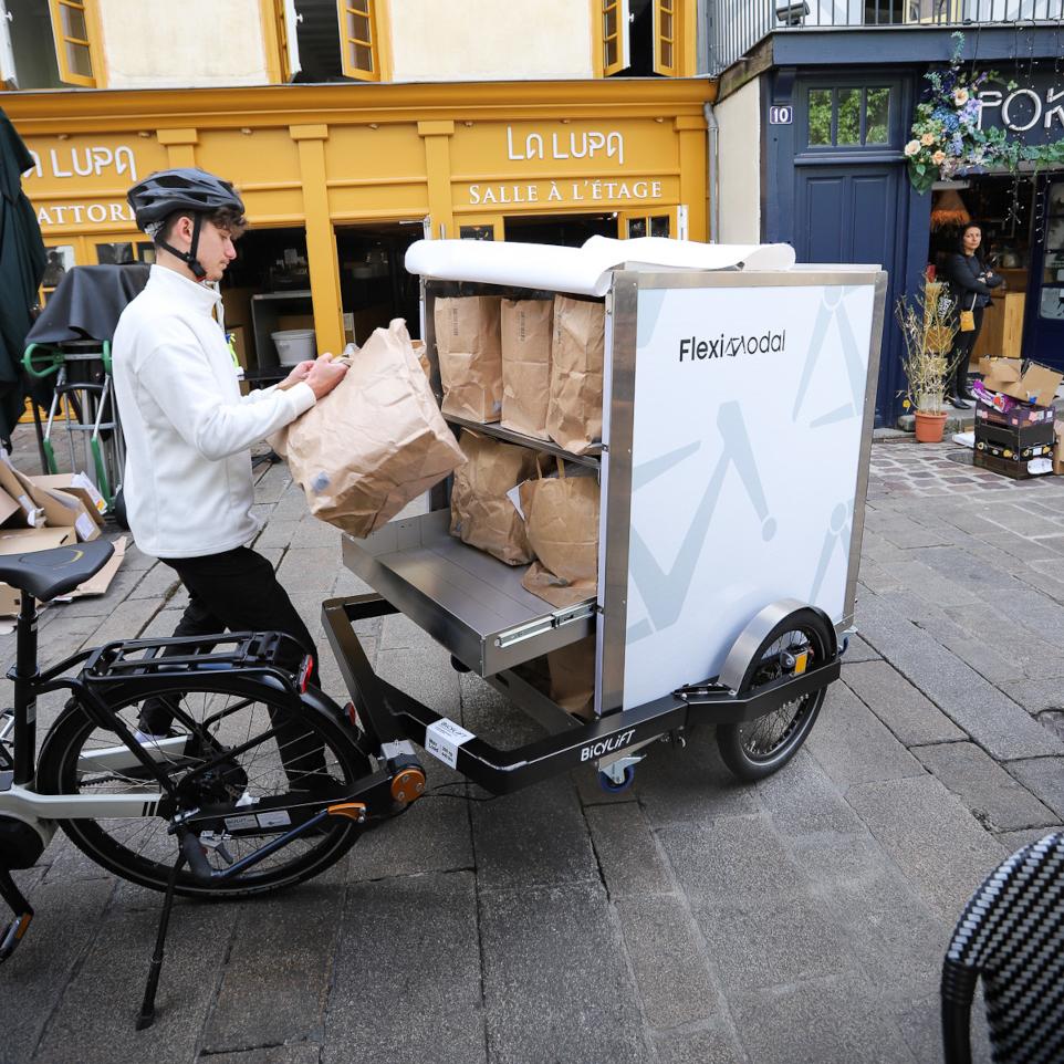Livreur alimentaire déchargeant le rack à bacs devant un restaurant de centre-ville