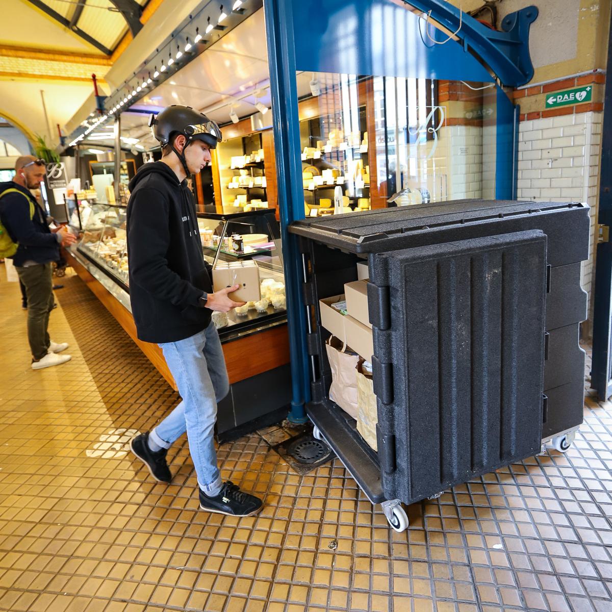 Conteneur Isotherme Roll O'City dans un marché couvert en train d'être chargé par un jeune homme avec un casque de vélo