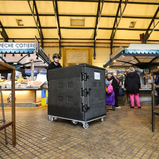 Jeune homme avec casque de vélo manipulant un Conteneur Isotherme à l'intérieur d'un marché couvert