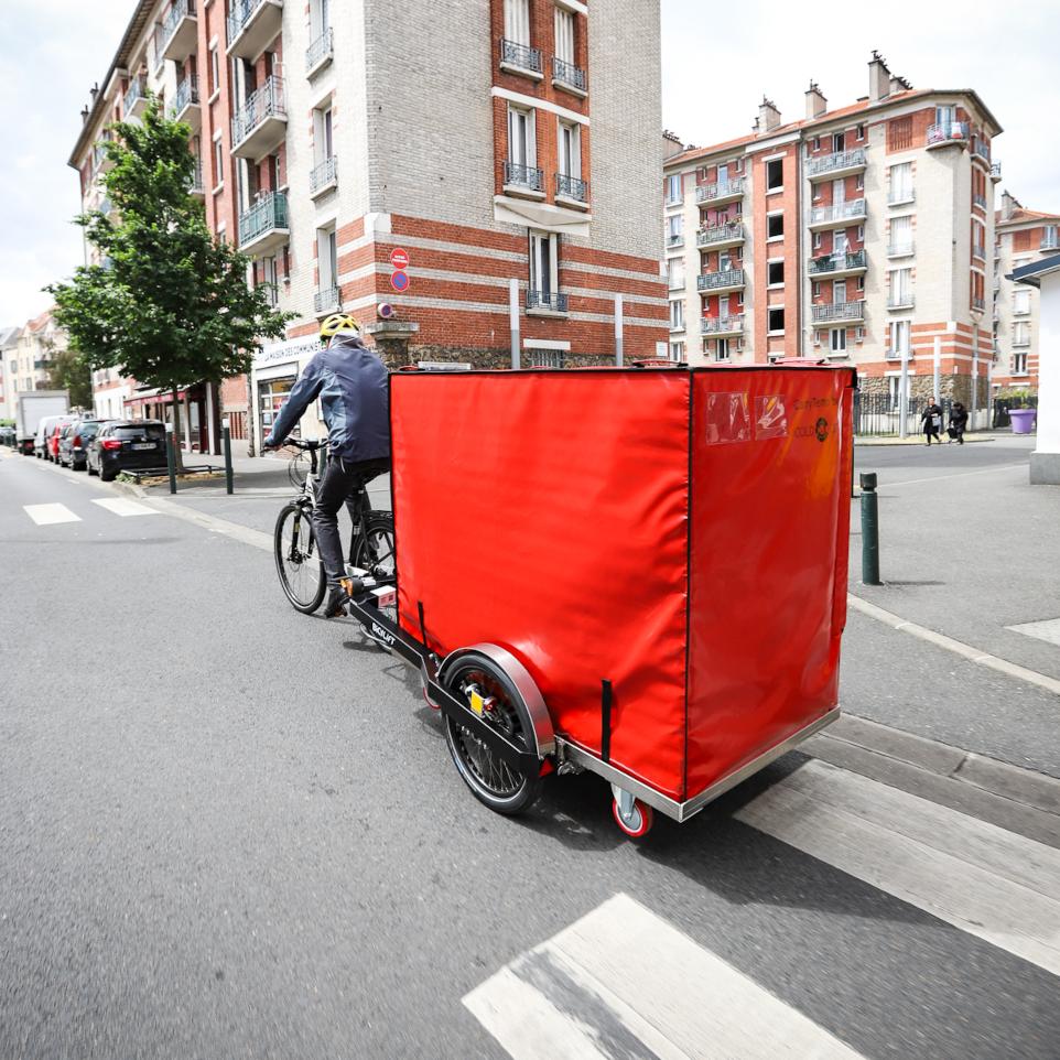 A bike courier pulling a BicyLift bike trailer with a XL9 Isothermal container with a Riese &amp;amp; Müller Nevo bicycle