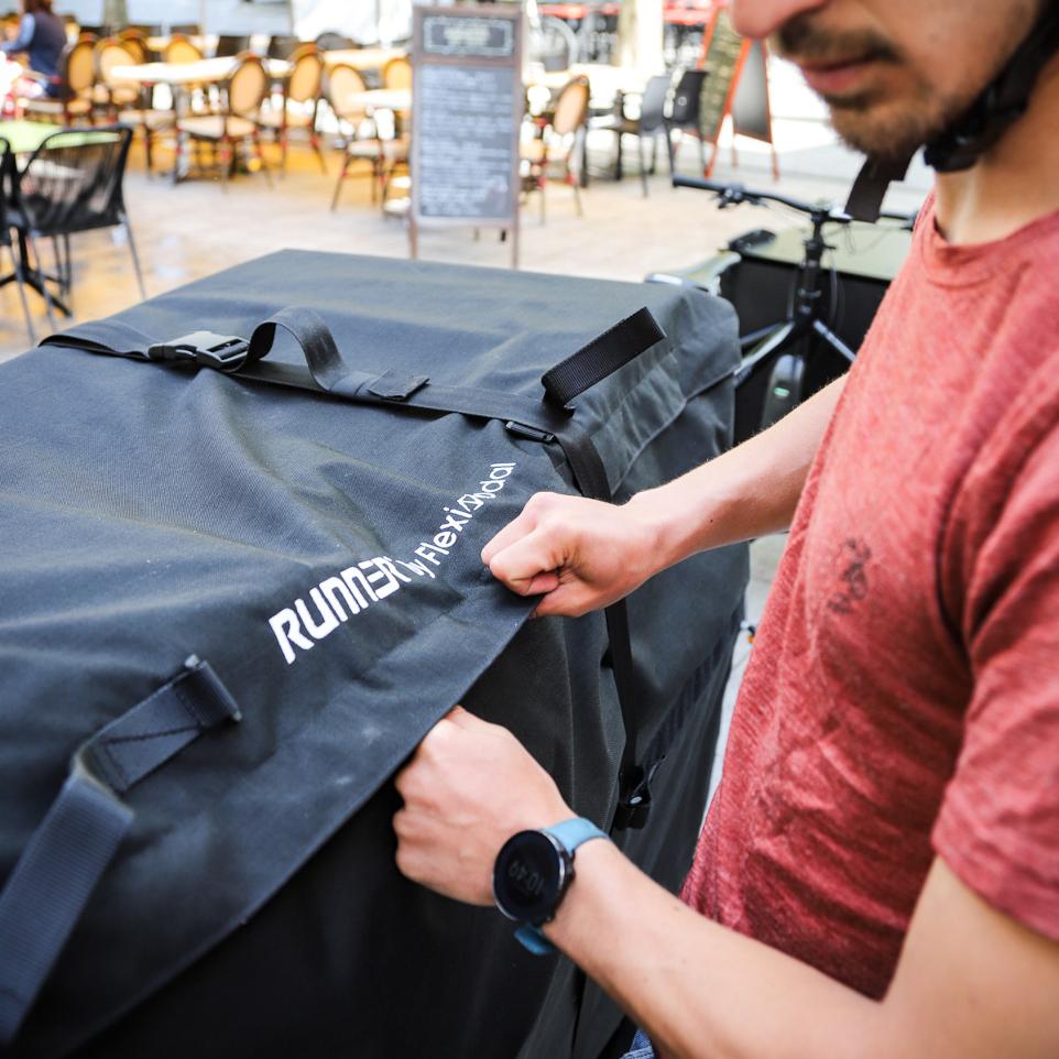 Bike courier opening a big black bag on which runner is written on it in white