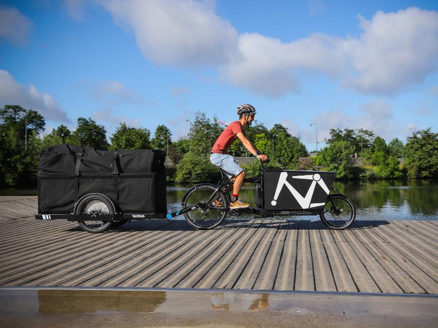 Bike courier on a Bullitt bike pulling a Runner with a MegaBag on top in front of a canal