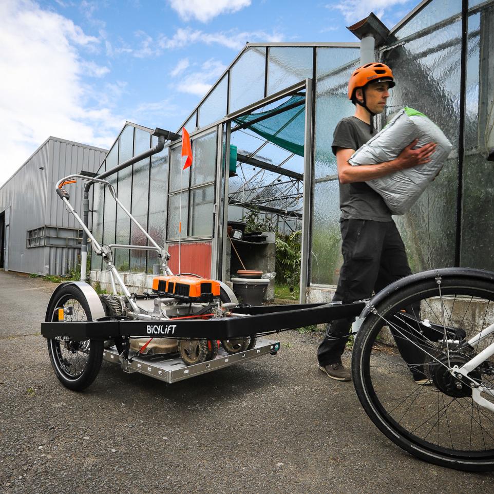 Paysagiste utilisant un plateau et une remorque vélo BicyLift pour transporter un tondeuse