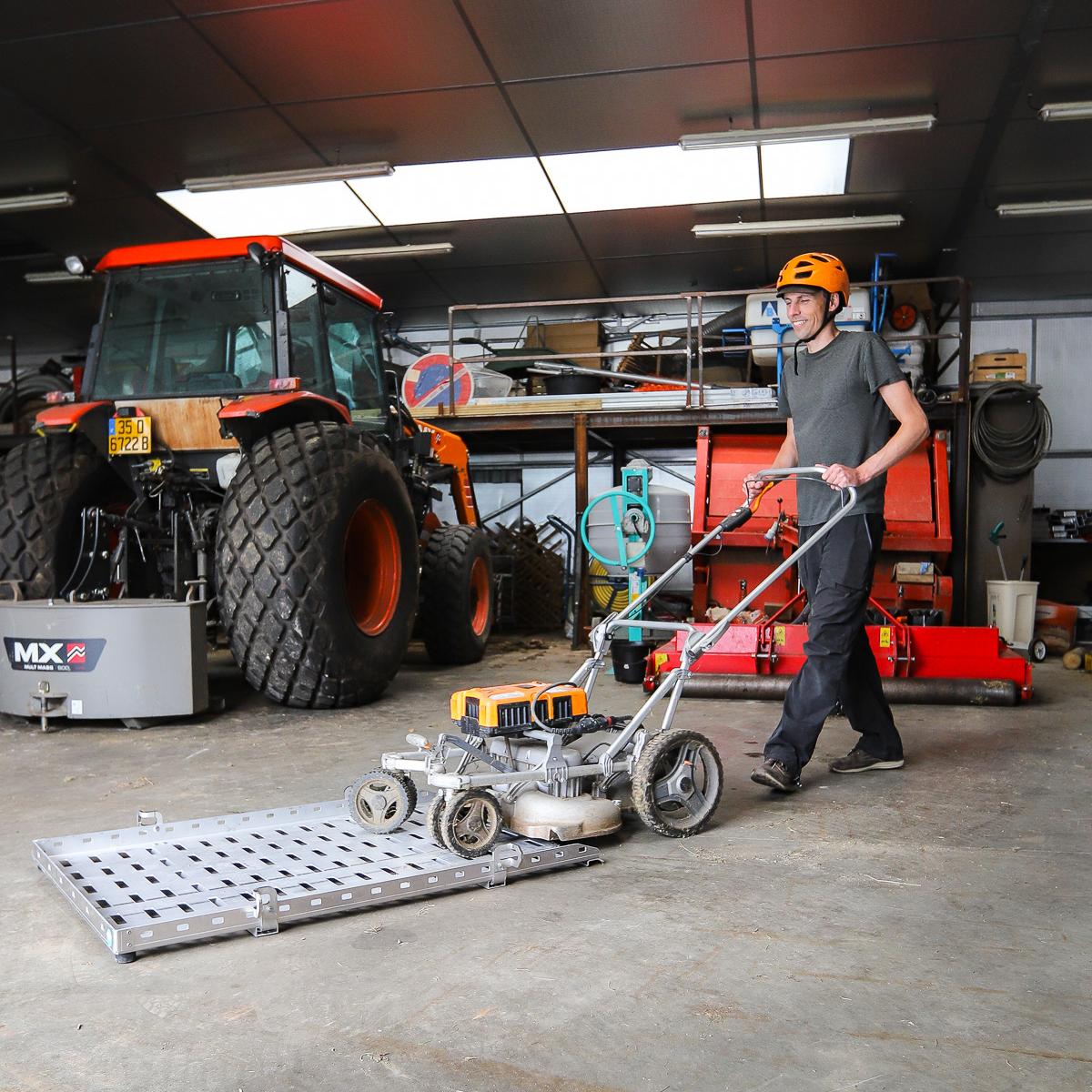 Person pushing a lawnmower on a flatbed in front of a tractor