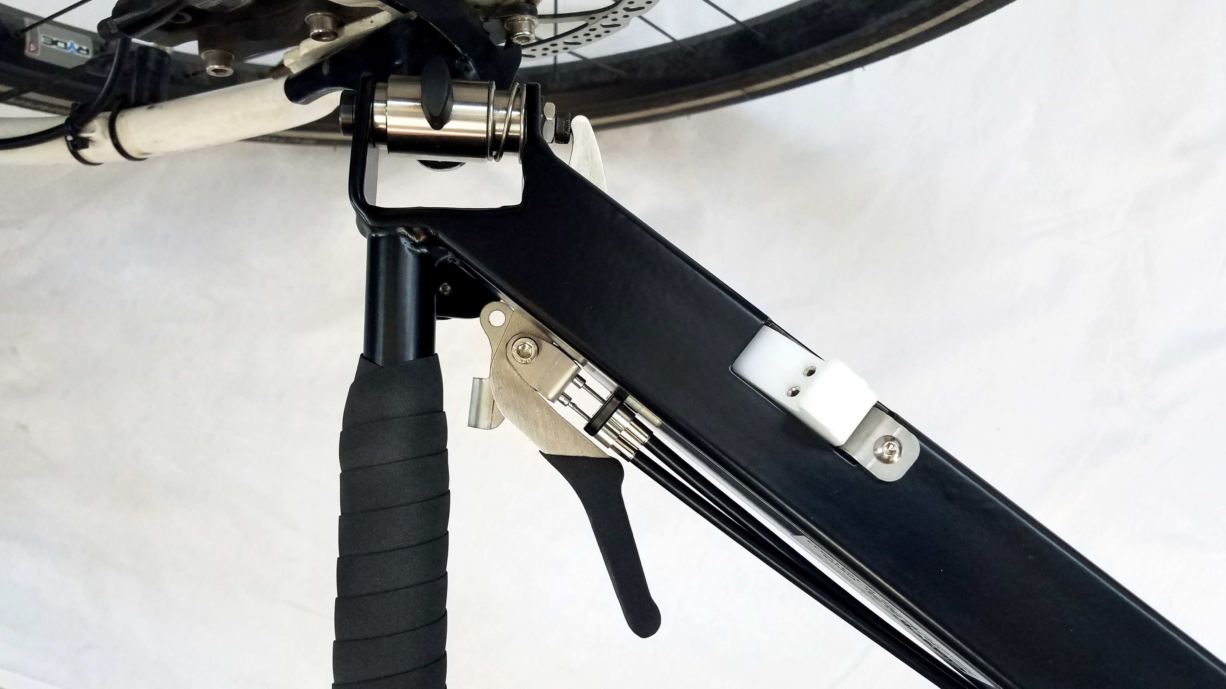 Metal frame attached to a hitch on the frame of a bike, white handle with two screws, metal handle with black protection and two cables 